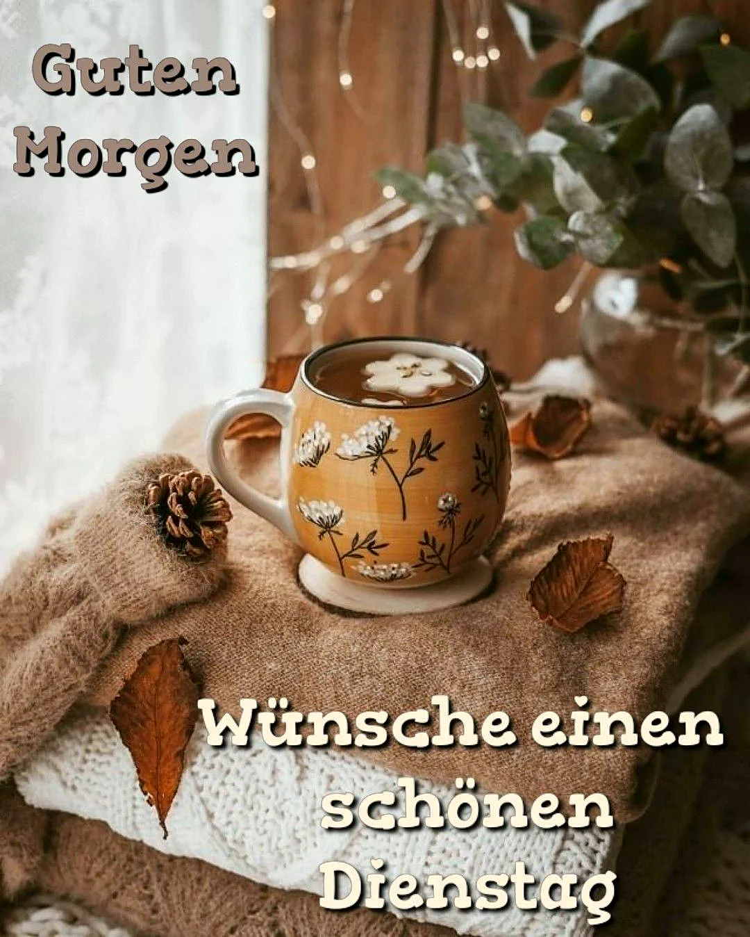 Gemütliche Tasse auf warmen Strickpullovern mit herbstlicher Dekoration. Tannenzapfen, trockene Blätter und sanfte Lichterkette schaffen eine einladende Atmosphäre. Perfekter Morgenmoment für einen produktiven Dienstag.
