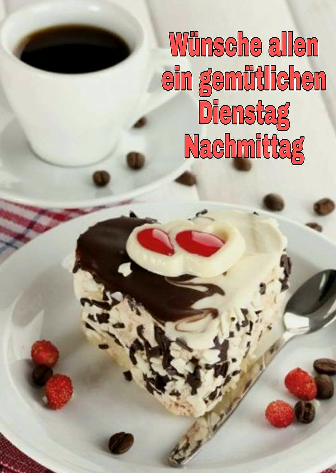 Ein Stück Schokoladen-Torte mit weißer Schokolade und roten Früchten auf einem weißen Teller, daneben ein Löffel, Kaffee in einer weißen Tasse im Hintergrund, auf einem roten Tischtuch