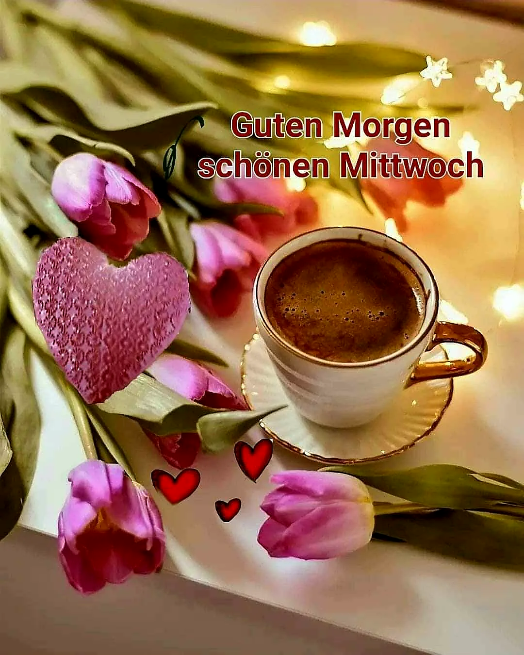 Nahaufnahme einer Kaffeetasse mit goldenem Rand, umgeben von pinken Tulpen und einem großen rosa Herz. Warme Lichter funkeln im verschwommenen Hintergrund, ergänzt durch kleine rote Herzen, ideal für einen gemütlichen Mittwochsgruß.