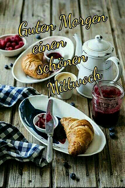 Ein rustikaler Holz-Tisch mit zwei Frühstücksplatten, Croissants, Marmelade, Tee und frischen Beeren. Guten Morgen, schönen Mittwoch.