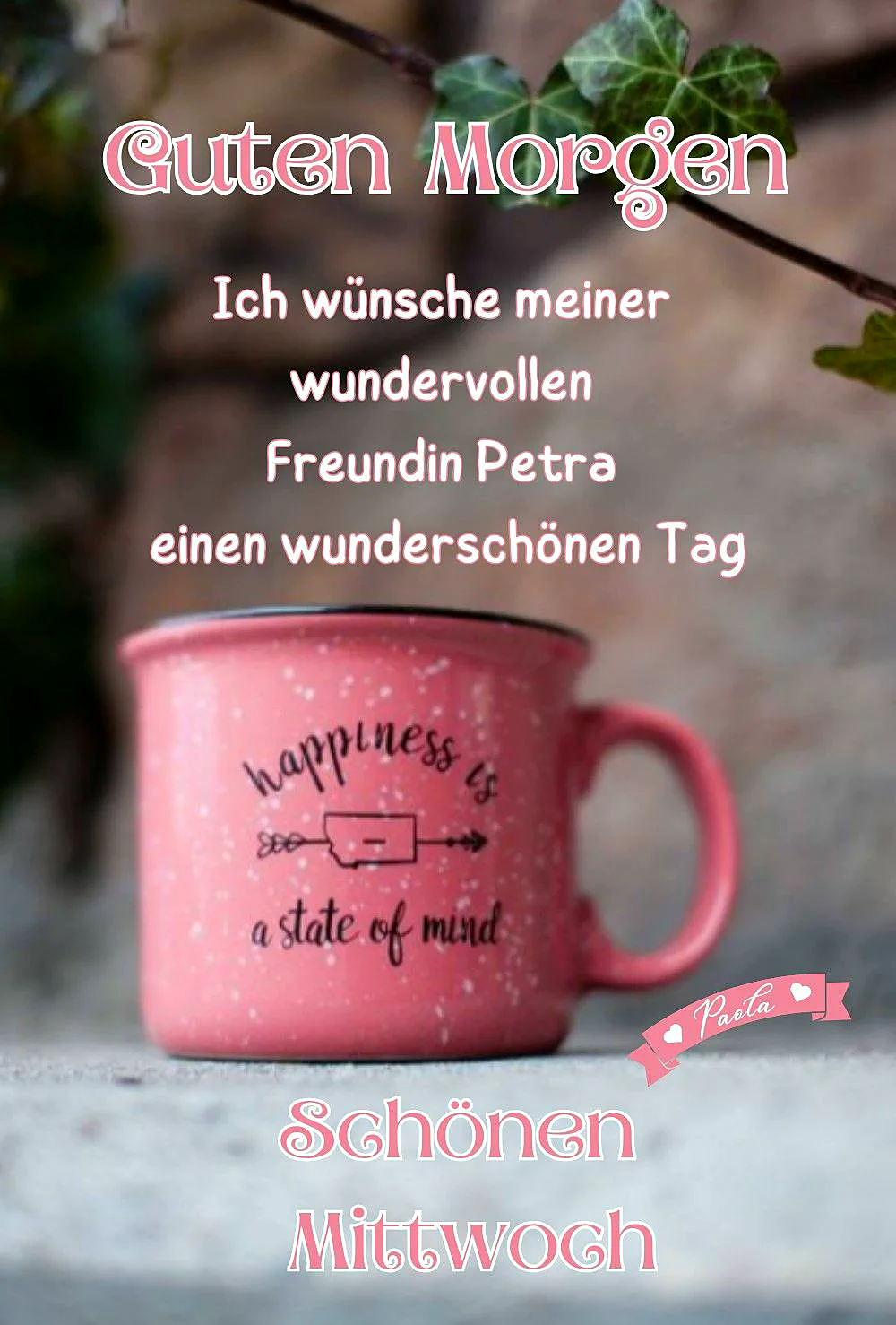 Ein rosa Kaffeebecher mit einem schwarzen Aufdruck, der sagt 'Happiness is a state of mind', auf einem grauen Untergrund, umgeben von grünen Blättern.
