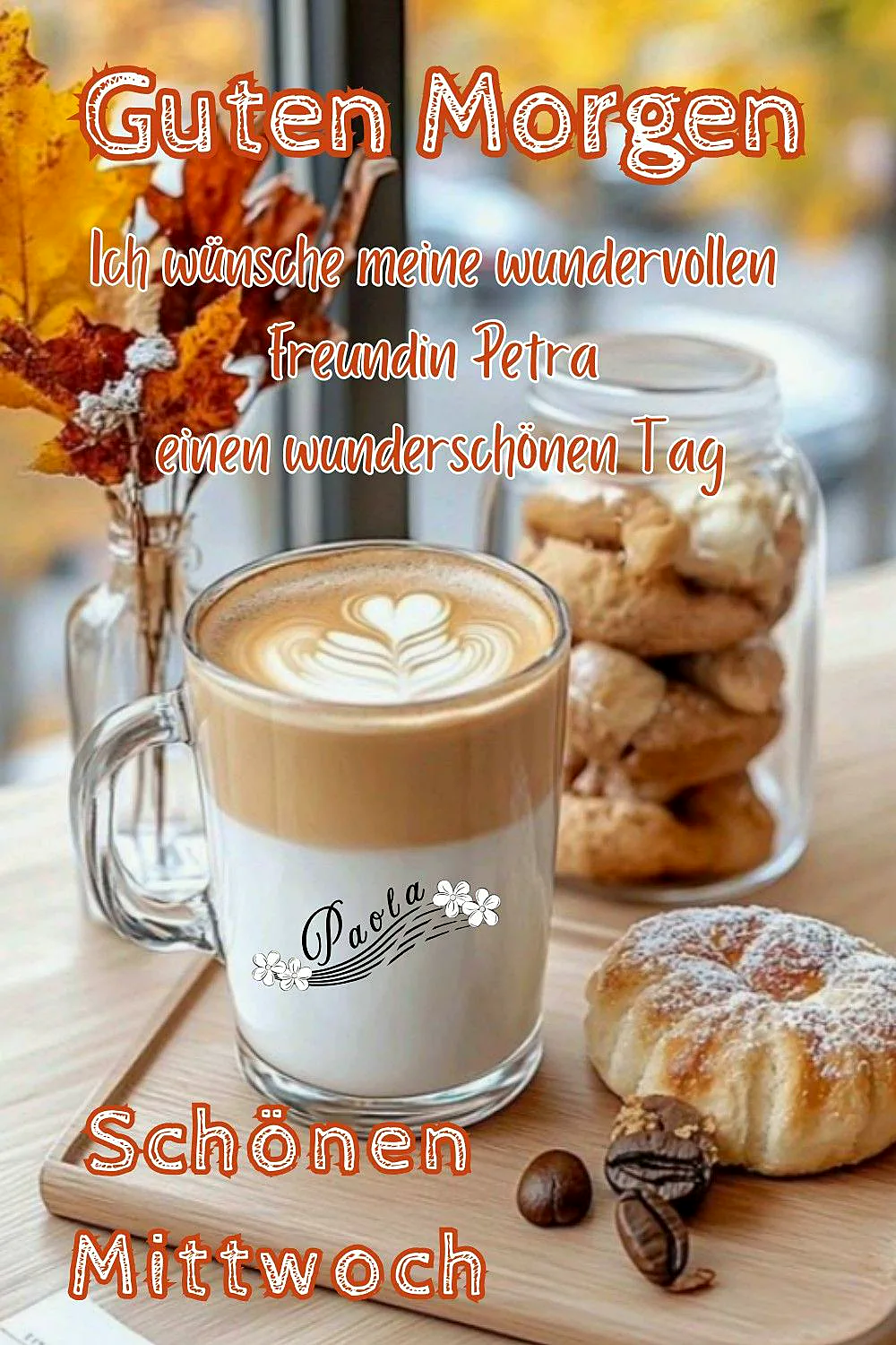 Ein Glas Kaffee mit Milch und einer Herz-Musterung auf dem Schaum, neben einem Glas mit Keksen, einem Kaffeebohnen und einem Donut auf einem Holzbrett, im Hintergrund Herbstblätter in einer Vase