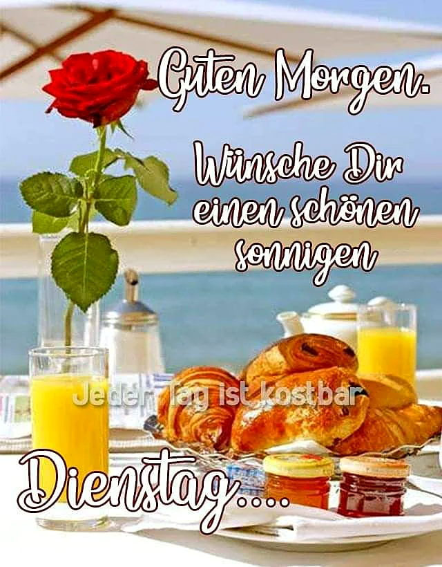Ein sommerliches Frühstück am Meer mit einer roten Rose, zwei Gläsern Orangensaft, frischen Croissants und Marmelade auf einem weißen Tisch. Dazu herzliche Dienstagswünsche für einen guten Start in den Tag.