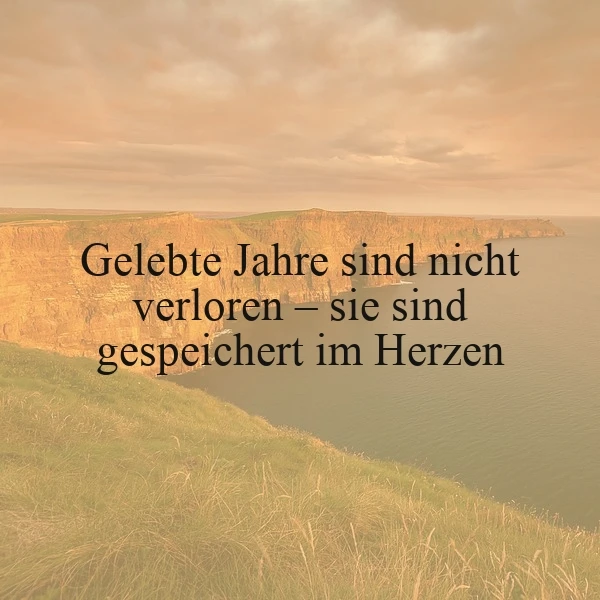 Ruhige Küstenlandschaft in goldenem Abendlicht, Klippen und weites Meer. Grasbewachsener Vordergrund. Der Spruch 'Gelebte Jahre sind nicht verloren – sie sind gespeichert im Herzen' vermittelt tiefe Besinnlichkeit und warme Geborgenheit.