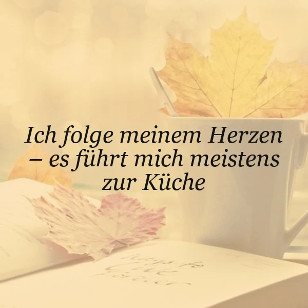 Ein herbstliches Stillleben mit einem offenen Buch, einem weißen Kaffeebecher, in dem gelbe und rosa Herbstblätter stecken. Der Kaffeebecher und das Buch liegen auf einem hellen Untergrund. Das Zitat 'Ich folge meinem Herzen - es führt mich meistens zur Küche' ist in schwarzer Schrift über das Bild gelegt.