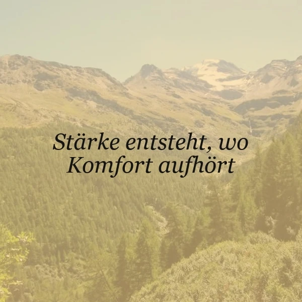 Ein Panorama einer dichten, grünen Waldlandschaft mit schroffen, teils schneebedeckten Bergen im Hintergrund. Der Himmel ist hell und wolkenlos. Im Vordergrund ist ein Zitat in schwarzer Schrift eingeblendet: 'Stärke entsteht, wo Komfort aufhört'.