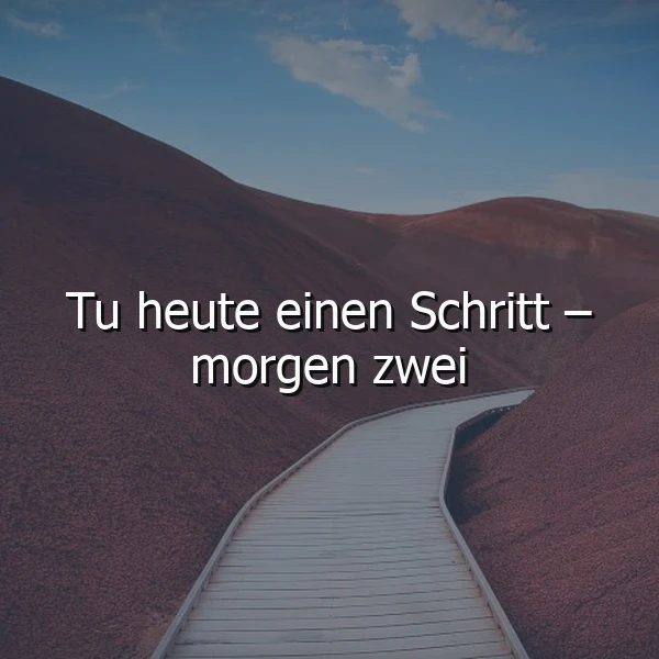 Ein Holzsteg bahnt sich seinen Weg durch sanfte, ockerfarbene Hügel unter einem klaren Himmel. Weiß prangt die motivierende Weisheit: "Tu heute einen Schritt – morgen zwei", ein Symbol für stetigen Fortschritt und neue Anfänge in ruhiger Landschaft.