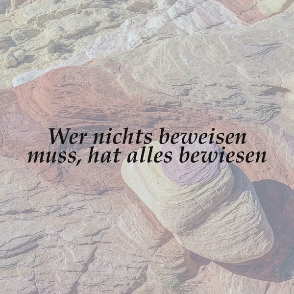 Ein Bild mit dem tiefgründigen Zitat „Wer nichts beweisen muss, hat alles bewiesen“ auf einem Hintergrund aus sanft geschwungenen, ockerfarbenen Felsformationen, die eine ruhige und nachdenkliche Atmosphäre schaffen.